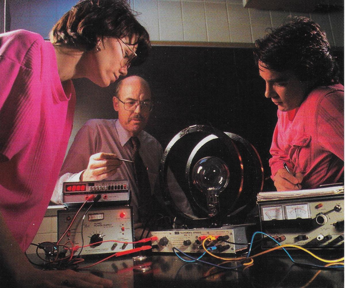 Three people looking at a light bulb in a coil